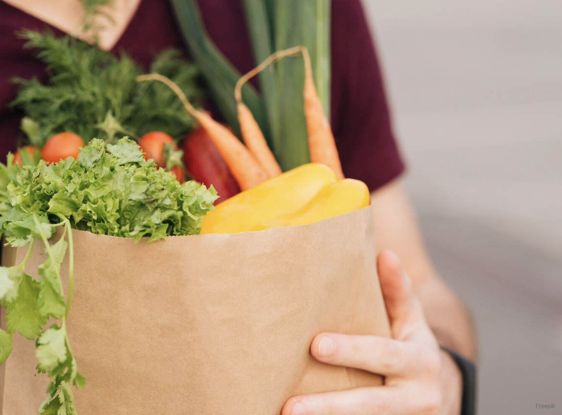 person holds paper bag with colorful vegetables inside